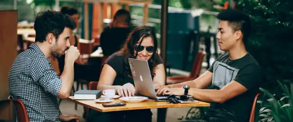 Pokolenie Z w kawiarni: młodzi ludzie pracują na laptopie, piją kawę i rozmawiają.